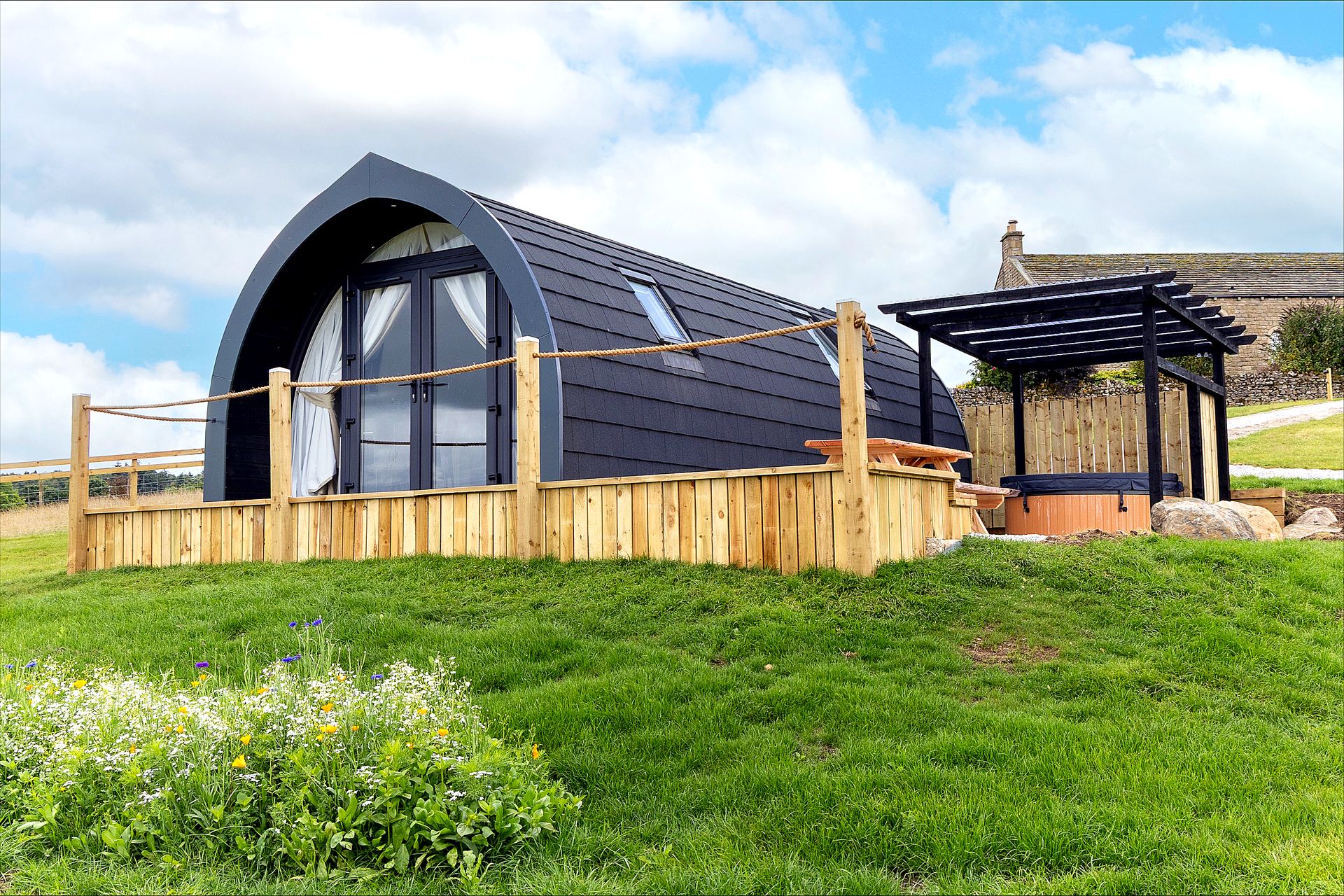 Curlew glamping pod exterior with pergola, hot tub and wildflower meadow
